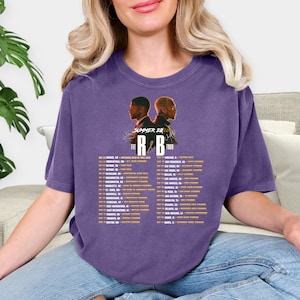 May include: Purple t-shirt featuring a graphic of two men's silhouettes and the text "Summer 2023" above "The R&B Tour". Below the graphic is a list of tour dates and locations in a gold color.