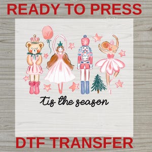May include: A DTF transfer sheet featuring a teddy bear in a crown, a ballerina, a nutcracker, and a mouse ballerina, all in pink and blue tones. The design includes stars, a balloon, a pine tree, and the black text 'tis the season'.