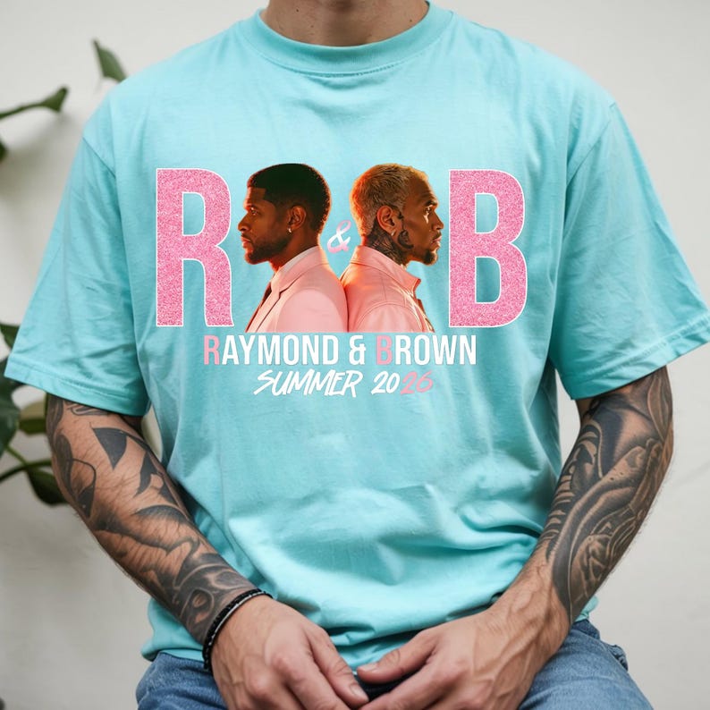 May include: A light blue t-shirt featuring the text "R&B" in pink glitter, with the words "Raymond & Brown Summer 2023" below. The shirt has a graphic of two men in profile, one in a pink suit and the other in a pink shirt.
