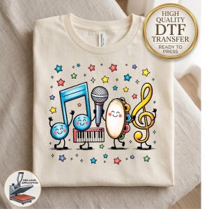 May include: A cream-colored t-shirt featuring a colorful graphic of anthropomorphic musical instruments including a blue musical note, a microphone, a keyboard, a tambourine, and a yellow treble clef, all surrounded by small multi-colored stars.