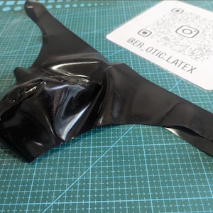 Può includere: Un capo in lattice nero con finitura lucida, forse un top o un pezzo di body. L'articolo è appoggiato su un tappetino da taglio verde. Sullo sfondo una scheda bianca con un codice QR e la scritta "@ER_OTIC.LATEX".