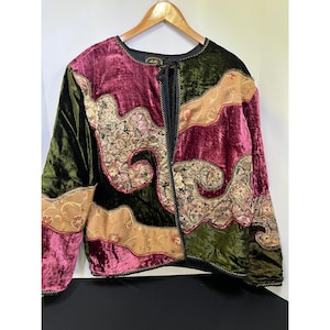 May include: A long-sleeved jacket featuring a patchwork design of deep burgundy and dark green velvet panels, interspersed with sections of tan fabric adorned with intricate floral embroidery. The front closure includes a black cord tie.