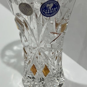 May include: A clear crystal vase with a cut design and gold accents. The vase has a flared top and a faceted body. It has a sticker that says "Czech Republic Crystal Heart Hand Made".