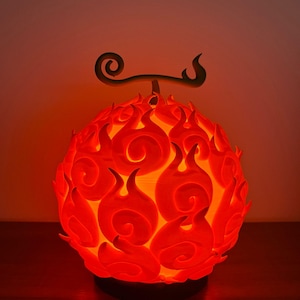 Peut inclure: Lampe rouge en forme de fruit avec des protubérances en forme de flammes. Elle possède une base sombre et un motif tourbillonnant décoratif. Le design évoque une esthétique enflammée, idéale pour une décoration thématique.