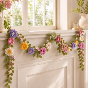 May include: A decorative garland featuring crocheted flowers in shades of purple, pink, yellow, and white, interspersed with green crocheted leaves and vines. The floral garland is draped across a white window ledge, showcasing intricate yarn textures.