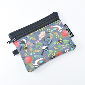 May include: A zipped pouch with a grey background featuring a colourful pattern of Australian wildlife, including birds, bees, butterflies, and flowers. The pouch has a black zip and a black leather-like trim.