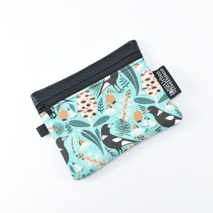 May include: A small, zipped pouch with a teal background featuring a pattern of black and white birds, tan seed pods, and white flowers. The top and zip are black, and a black tag reads "Urban Treehouse".