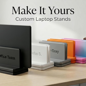 Op de afbeelding: Een collectie op maat gemaakte laptopstandaards in diverse kleuren, waaronder zwart, wit, grijs, oranje, roze en bruin. Elke standaard heeft een rechthoekig ontwerp met een basis en een achterpaneel. Tekst op de standaards luidt "Office Team", "John D.", "Gray" en "creative Hub."