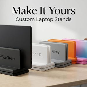 May include: A collection of custom laptop stands in various colors, including black, white, gray, orange, and pink. The stands have a rectangular design with a base and a back panel. Text on the stands reads "Office Team", "John D.", and "Gray". The logo for "X3N FORGE" is also visible.