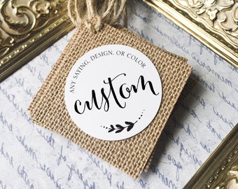 Pode incluir: Uma etiqueta personalizada com a palavra "custom" em escrita elegante, rodeada por um design floral. A etiqueta está sobre um quadrado de serapilheira, com uma rosa branca e uma moldura dourada no fundo. O texto na etiqueta diz "ANY SAYING, DESIGN, OR COLOR."