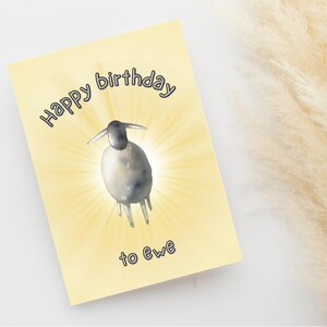 以下が含まれることがあります： 「Happy birthday to ewe」のテキストが入った黄色の誕生日カード。黒い頭と白い体を持つ羊の水彩イラストが、黄色のサンバーストを背景に描かれています。