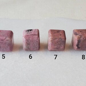 May include: Four pink and white, cube-shaped, polished stones with black veins. The stones are numbered 5 through 8.