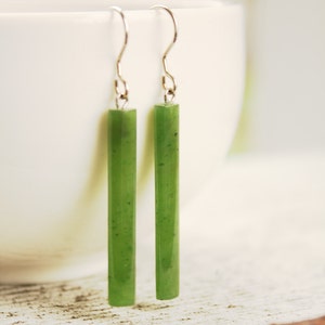 May include: A pair of dangle earrings with long, green jade stone bars hanging from silver hooks.