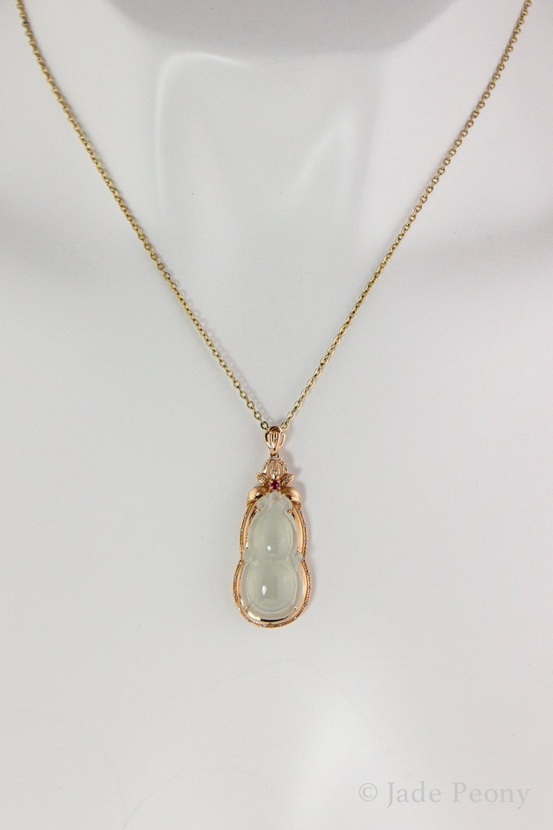 Puede incluir: Un collar de cadena de oro con un colgante de calabaza de jade. El colgante est&aacute; engastado en un marco de oro con una peque&ntilde;a piedra roja en la parte superior.