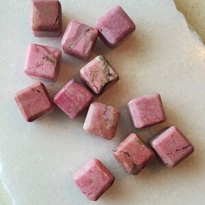 May include: A collection of pink and white polished rhodochrosite gemstone cubes. The cubes are various sizes and have a natural, rough texture.