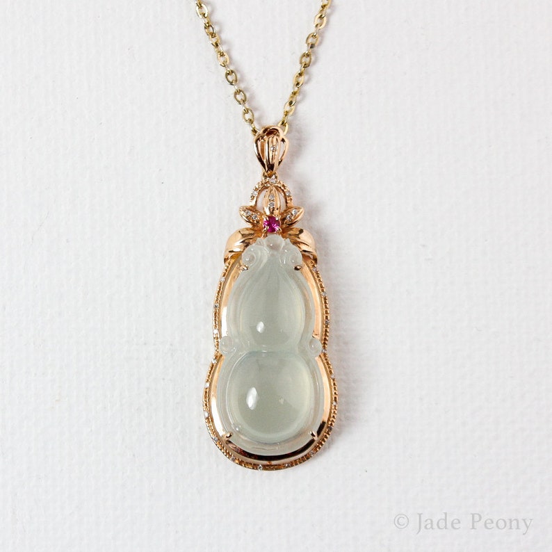 Puede incluir: Un collar con un colgante de jade con dise&ntilde;o de calabaza, engastado en oro rosa con diamantes y una piedra preciosa rosa. El colgante cuelga de una delicada cadena de oro.