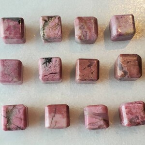 May include: Twelve pink and gray square-shaped polished stones. The stones have a natural, rough texture and are arranged in three rows of four.