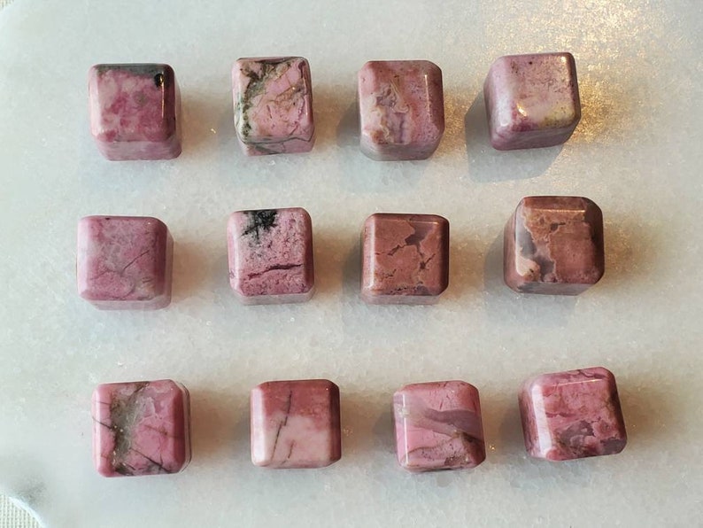 May include: Twelve pink and gray square-shaped polished stones. The stones have a natural, rough texture and are arranged in three rows of four.