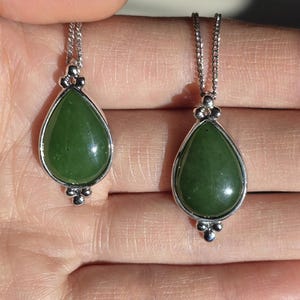 May include: Two jade teardrop pendants on silver chains. The green jade stones are set in silver bezels with decorative silver accents. The pendants are displayed against a neutral background.