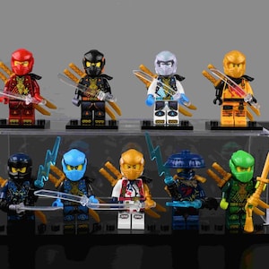 May include: A collection of eight Lego Ninjago minifigures, each with unique color schemes and accessories. The figures are displayed on individual black bases, with weapons like swords and lightning bolts. The color palette includes red, black, white, yellow, blue, and green.