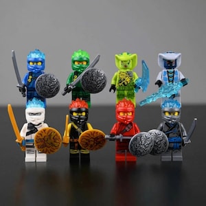 May include: A collection of eight colorful ninja action figures. Each figure is holding a weapon and a shield. The figures are in various colors, including blue, green, red, and white. The figures are standing on a dark surface.