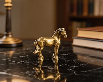 Puede incluir: Una pequeña figura de caballo de pie hecha de un material metálico de tono dorado. El caballo se muestra de perfil con una crin y una cola texturizadas, con una superficie reflectante que crea una imagen especular sobre la base oscura.
