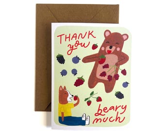 Op de afbeelding: Een wenskaart met een lichtgroene achtergrond met een bruine beer en een hond die bessen eten. De tekst THANK YOU beary much staat in het rood. De beer houdt rode bessen vast, terwijl de hond een geel shirt en een blauwe broek draagt.