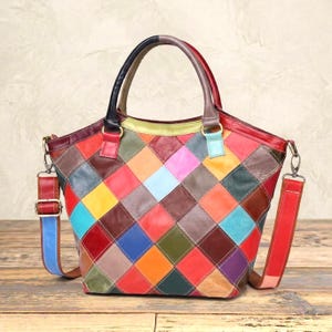 Op de afbeelding: Een veelkleurige leren handtas met een ruitvormig patchworkpatroon in tinten rood, blauw, geel, groen, oranje en paars. De tas is voorzien van twee handvatten, een afneembare schouderriem en goudkleurige metalen hardware.
