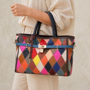 May include: A colorful patchwork tote bag with a geometric diamond pattern. The bag features a blue strap, black handles, and a gold-colored lock. The bag is made of leather and has a variety of colors including red, yellow, and blue.