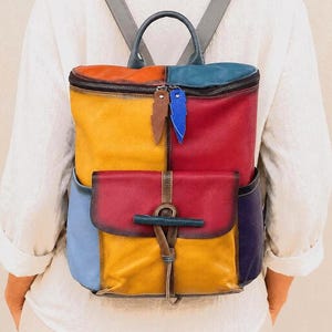 Könnte beinhalten: Ein mehrfarbiger Lederrucksack mit Patchwork-Design in den Farben Gelb, Rot, Blau und Violett. Der Rucksack verfügt über einen Tragegriff, verstellbare Schultergurte, ein Hauptfach mit Reißverschluss und eine Vordertasche mit Klappenverschluss.