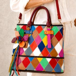 May include: A multi-coloured handbag featuring a patchwork diamond pattern in shades of red, blue, green, yellow, pink, and brown. The bag includes two dark red top handles, a detachable shoulder strap, and a decorative leather flower charm.