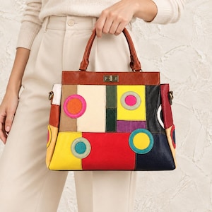 May include: A structured handbag featuring a patchwork design of multi-colored leather panels in red, yellow, black, green, and cream. The bag includes circular appliqués in pink, teal, and yellow, a brown leather handle, and a gold-tone metal turn-lock.