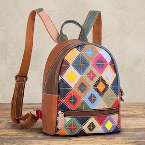 Puede incluir: Una mochila con un patrón de rombos multicolor en el panel frontal, confeccionada con paneles de cuero texturizado en marrón, azul, rojo, amarillo y rosa. Incluye un asa superior, un bolsillo frontal con cremallera y correas ajustables.