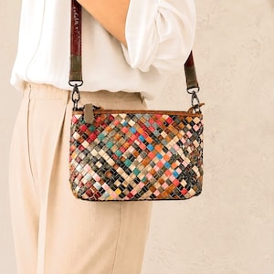May include: A rectangular crossbody bag featuring a multi-colored woven pattern of small leather squares in shades of red, blue, green, yellow, and black. The bag includes a brown leather zipper pull and a detachable shoulder strap with metal clips.