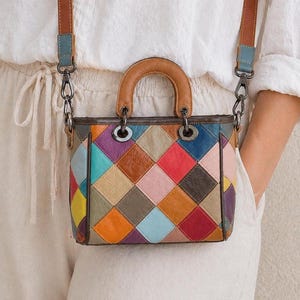 May include: A colorful patchwork leather handbag with a top handle and a detachable shoulder strap. The bag features a variety of diamond-shaped patches in shades of blue, pink, orange, and brown. The handle and strap are brown leather.