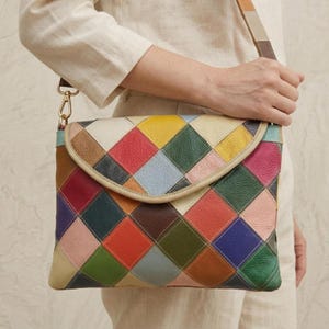 Könnte beinhalten: Bunte Patchwork-Umhängetasche aus Leder mit Klappverschluss. Die Tasche hat quadratische Patches in verschiedenen Farben, darunter Rot, Gelb, Blau und Grün. Sie hat einen langen, verstellbaren Riemen und goldfarbene Hardware.