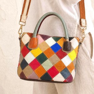 Peut inclure: Un sac à main au motif patchwork multicolore composé de pièces de cuir en forme de losange dans des tons de rouge, jaune, bleu, orange, vert, blanc et marron. Il possède deux anses supérieures vert clair et une bandoulière en tissu marron.