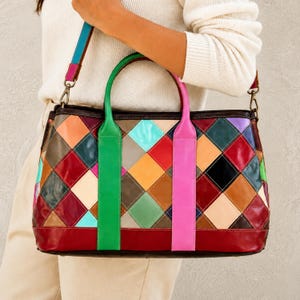 Op de afbeelding: Een kleurrijke patchwork leren tote bag met een rode basis. De tas heeft ruitvormige patches in verschillende kleuren, groene en roze handvatten en een veelkleurige schouderriem.