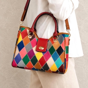 May include: A multi-colored handbag featuring a patchwork diamond pattern in shades of red, yellow, blue, green, orange, pink, and grey. The bag includes two red top handles, a detachable brown shoulder strap, and a red flap closure with a gold-tone turn-lock.