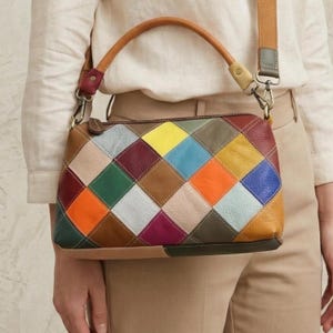 May include: A colorful patchwork leather handbag with a brown handle and a detachable shoulder strap. The bag features a geometric pattern of various colored squares, including red, yellow, blue, and green. The bag is a crossbody style.
