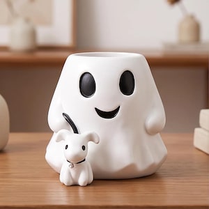May include: A white ceramic ghost-shaped planter or container featuring a smooth finish, black oval eyes, and a curved black mouth. A small white dog figurine with a black collar and a silver-toned charm is attached to the front of the ghost.