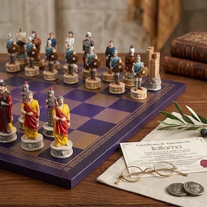 May include: A chess set featuring hand-painted Roman-themed pieces on a purple and gold chequered board. The set includes a certificate of authenticity from Italfama, a pair of gold-rimmed spectacles, and two metal coins resting on a linen cloth.