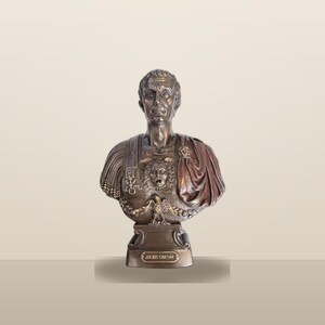 Peut inclure: Un buste de couleur bronze repr&eacute;sentant Jules C&eacute;sar, dot&eacute; d'une armure d&eacute;taill&eacute;e avec un embl&egrave;me central en forme de t&ecirc;te de M&eacute;duse et un motif d'aigle. La figure porte une cape drap&eacute;e sur une &eacute;paule et repose sur un socle avec une plaque JULIUS CAESAR.