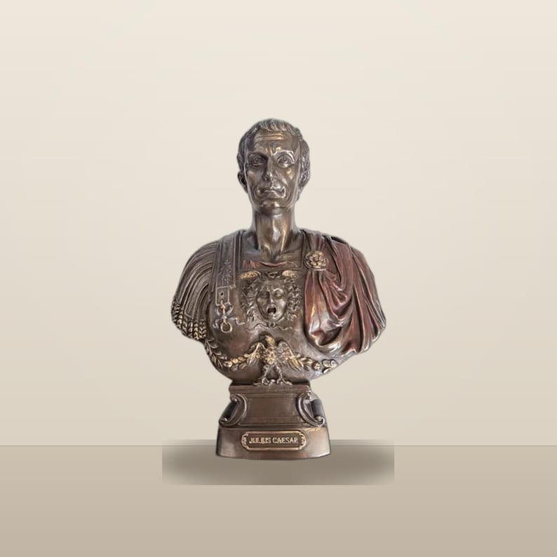 Peut inclure: Un buste de couleur bronze repr&eacute;sentant Jules C&eacute;sar, dot&eacute; d'une armure d&eacute;taill&eacute;e avec un embl&egrave;me central en forme de t&ecirc;te de M&eacute;duse et un motif d'aigle. La figure porte une cape drap&eacute;e sur une &eacute;paule et repose sur un socle avec une plaque JULIUS CAESAR.