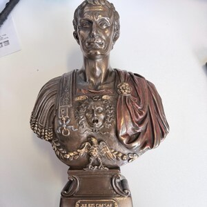Peut inclure: Un buste de couleur bronze repr&eacute;sentant Jules C&eacute;sar avec des traits du visage d&eacute;taill&eacute;s, une cuirasse orn&eacute;e d'une t&ecirc;te de Gorgone et d'un aigle, et une cape drap&eacute;e sur l'&eacute;paule. La base comporte une plaque avec le texte JULIUS CAESAR.