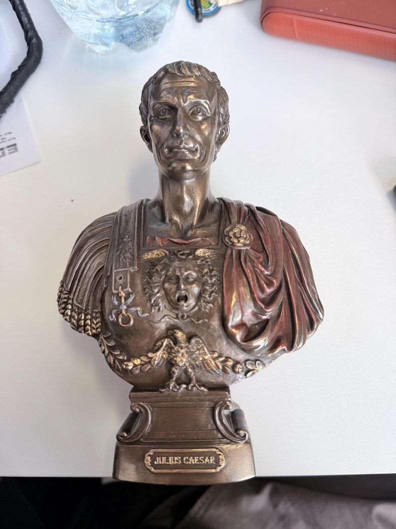 Peut inclure: Un buste de couleur bronze repr&eacute;sentant Jules C&eacute;sar avec des traits du visage d&eacute;taill&eacute;s, une cuirasse orn&eacute;e d'une t&ecirc;te de Gorgone et d'un aigle, et une cape drap&eacute;e sur l'&eacute;paule. La base comporte une plaque avec le texte JULIUS CAESAR.