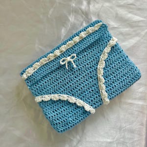 Peut inclure: Une pochette crochetée bleu clair avec une bordure blanche et un petit nœud. Le sac rectangulaire présente un motif ajouré délicat. La bordure blanche est festonnée, ajoutant un élément décoratif à l'accessoire fait à la main.