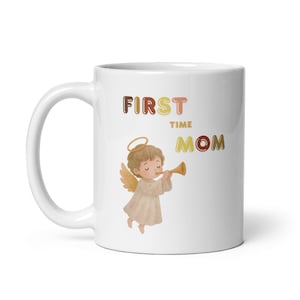 Puede incluir: Taza de cerámica blanca con el texto "FIRST TIME MOM" en letras marrones, rosas y amarillas. Un ángel de dibujos animados con alas y un halo toca la trompeta. La taza tiene un asa curva y está diseñada para bebidas calientes.