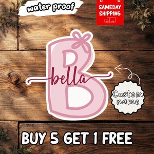 May include: A pink sticker in the shape of the letter "B" with the name "bella" in cursive. The sticker has a bow at the top and is labeled "water proof". A separate tag says "Custom name".