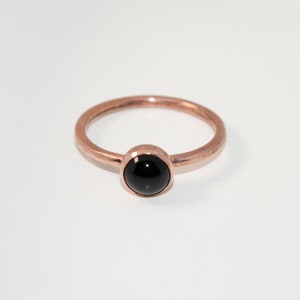 May include: A simple rose gold ring with a black gemstone.